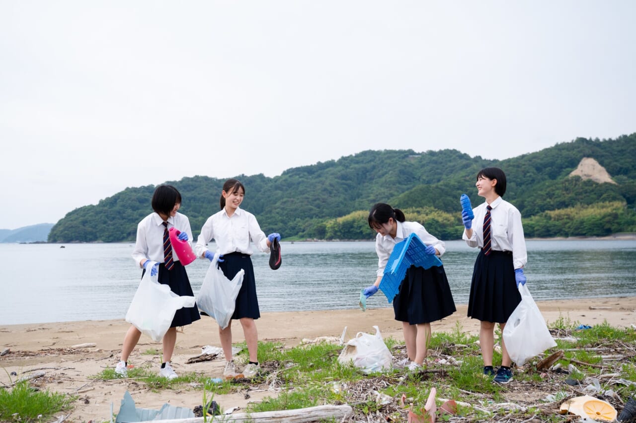海辺でゴミ拾いをする女子高生たち